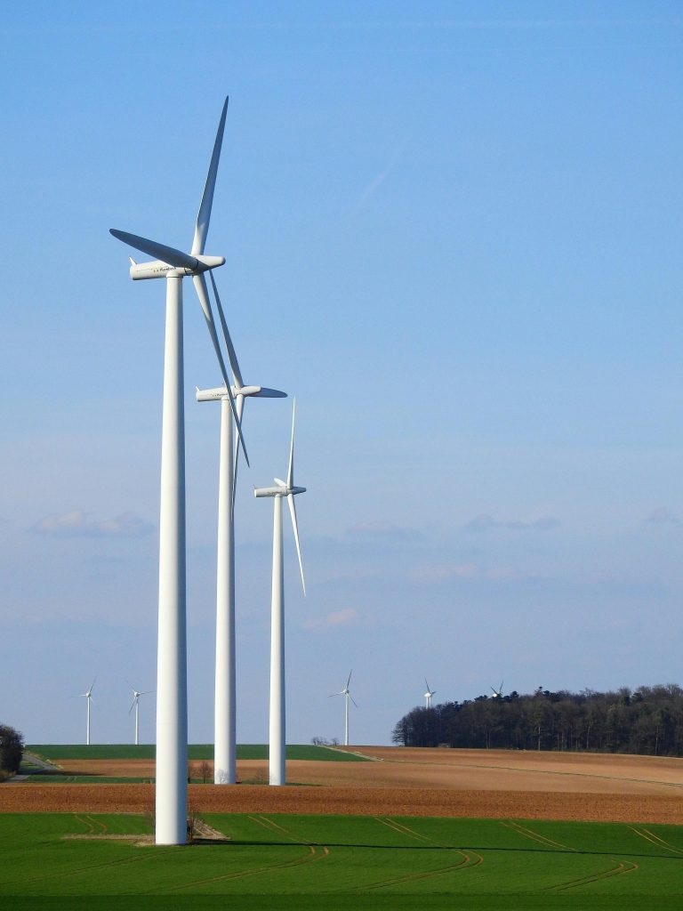 Row of wind turbines in a rural area, generating renewable energy under a blue sky.
